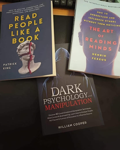 Three books on a dark surface titled 'Read People Like a Book', 'The Art of Reading Minds', and 'Dark Psychology Manipulation'.